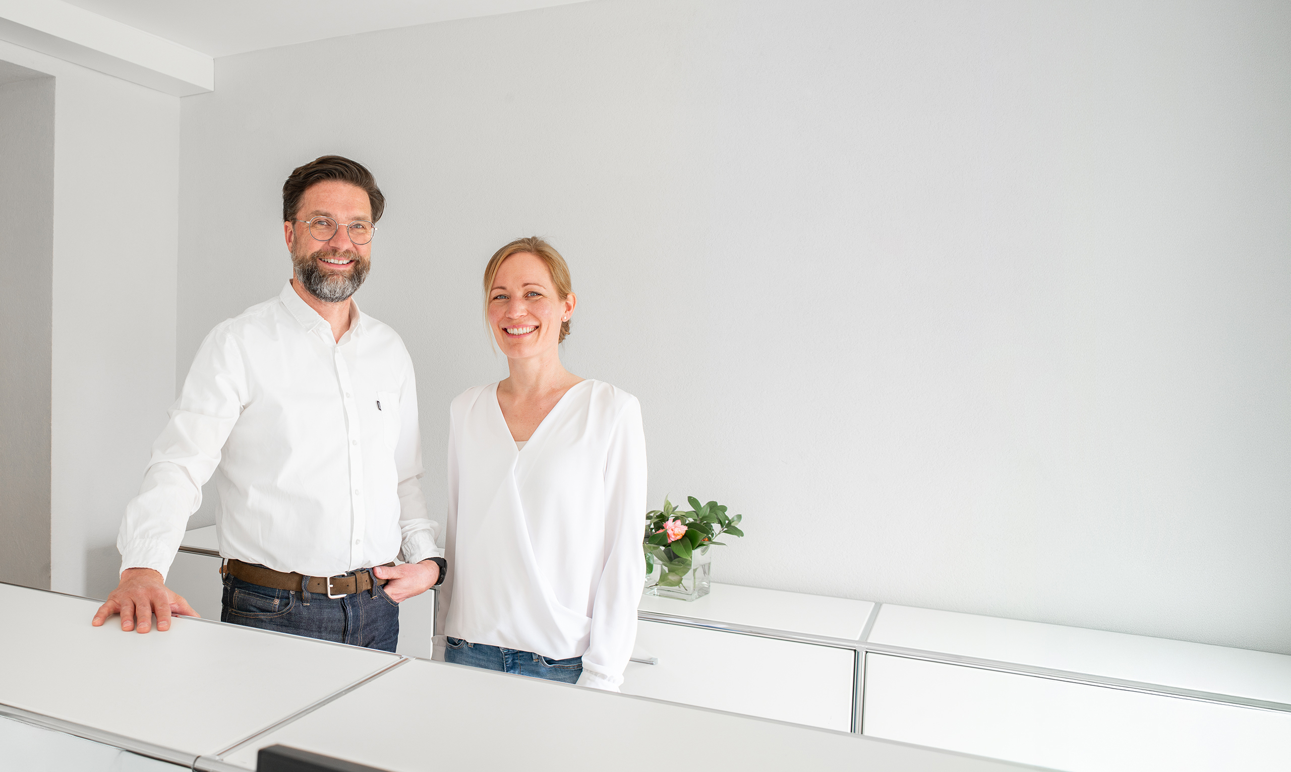 Stephan Groothuisen und Dr. med. Lisa Schönbrunn stehen am Empfang und lächeln in die Kamera